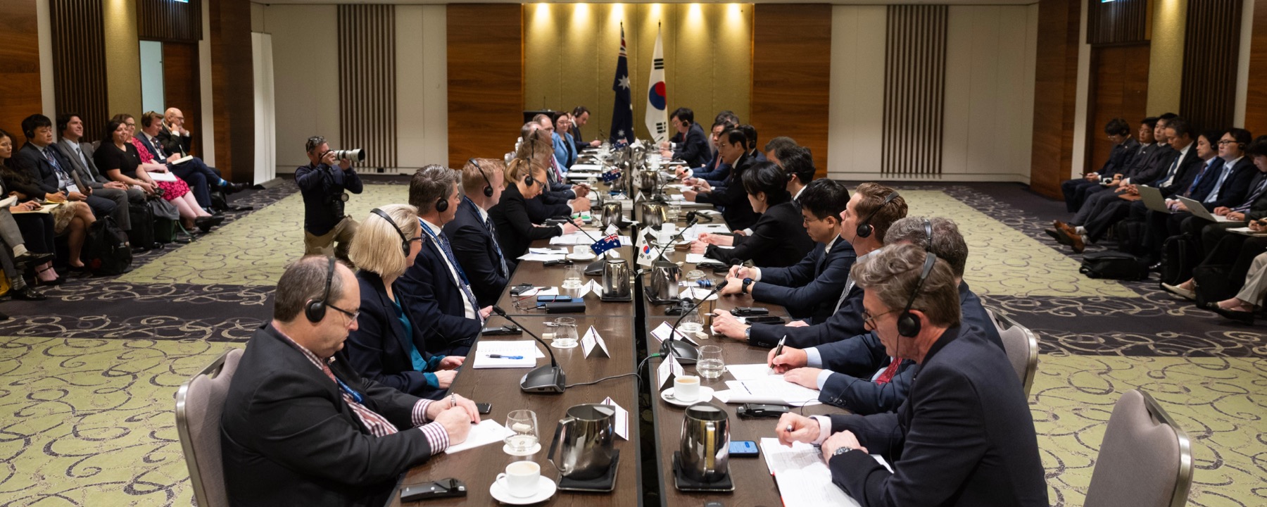 Australian and Korean delegates at a bilateral roundtable, seated either side of a long table with national flags at its head